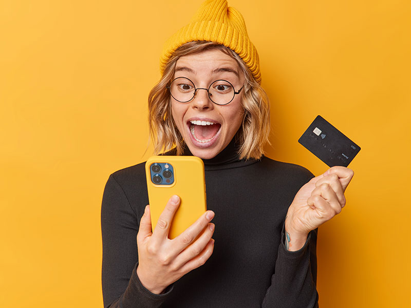 mulher feliz com celular na mao e cartao de credito